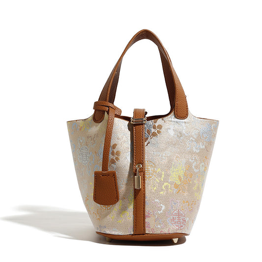 Refined printed woven bucket tote bag with brown leather handles and lock charm.